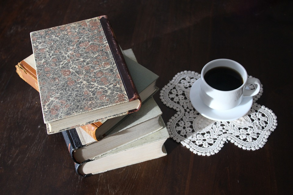 Ein Foto mit einer Tasse Kaffee und einem Stapel Bücher auf einem Tisch als Metapher für das Lernen.