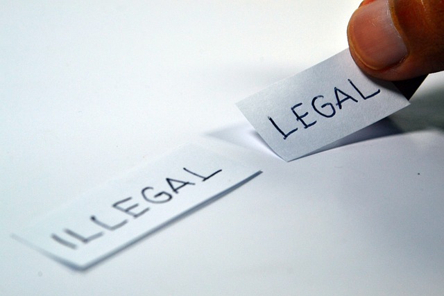 The picture shows how a small strip of paper with the word illegal written in capital letters is lying on a white table. To the right of it, someone is laying another strip with the word legal.